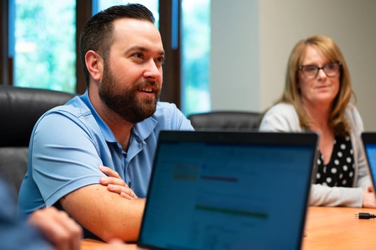 Schneller-employees-sitting-at-table-collaborating-in-a-meeting-using-laptop-devices