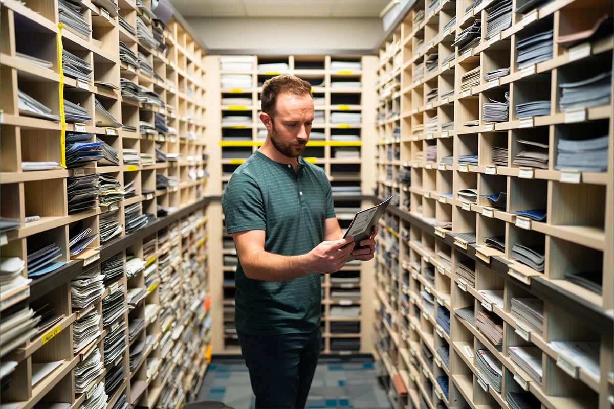 an-employee-standing-in-a-room-surrounded-by-shelves-filled-with-design-swatches-analyzing-a-document