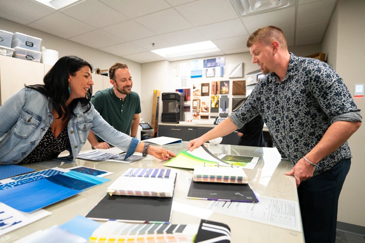 schneller-employees-leaning-over-a-table-engaged-in-conversation-looking-at-color-swatch-books-sprawled-across-the-table