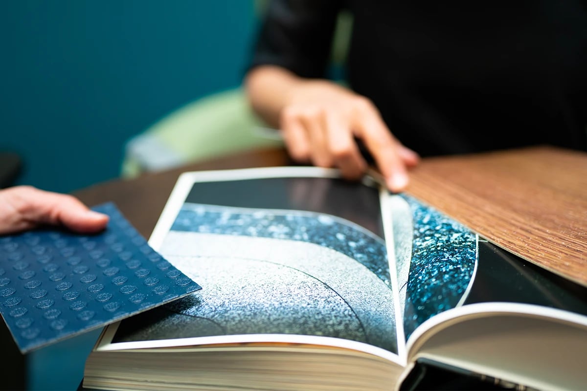 detailed-view-of-a-design-swatch-book-flipped-open-with-two-employees-holding-up-contrasting-aircraft-interior-material-swatches