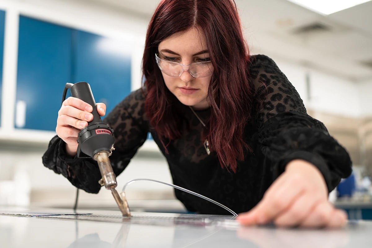 schneller-engineer-focused-wearing-safety-goggles-leaning-over-a-flat-surface-working-on-customizing-aircraft-interior-material-with-a-handheld-tool