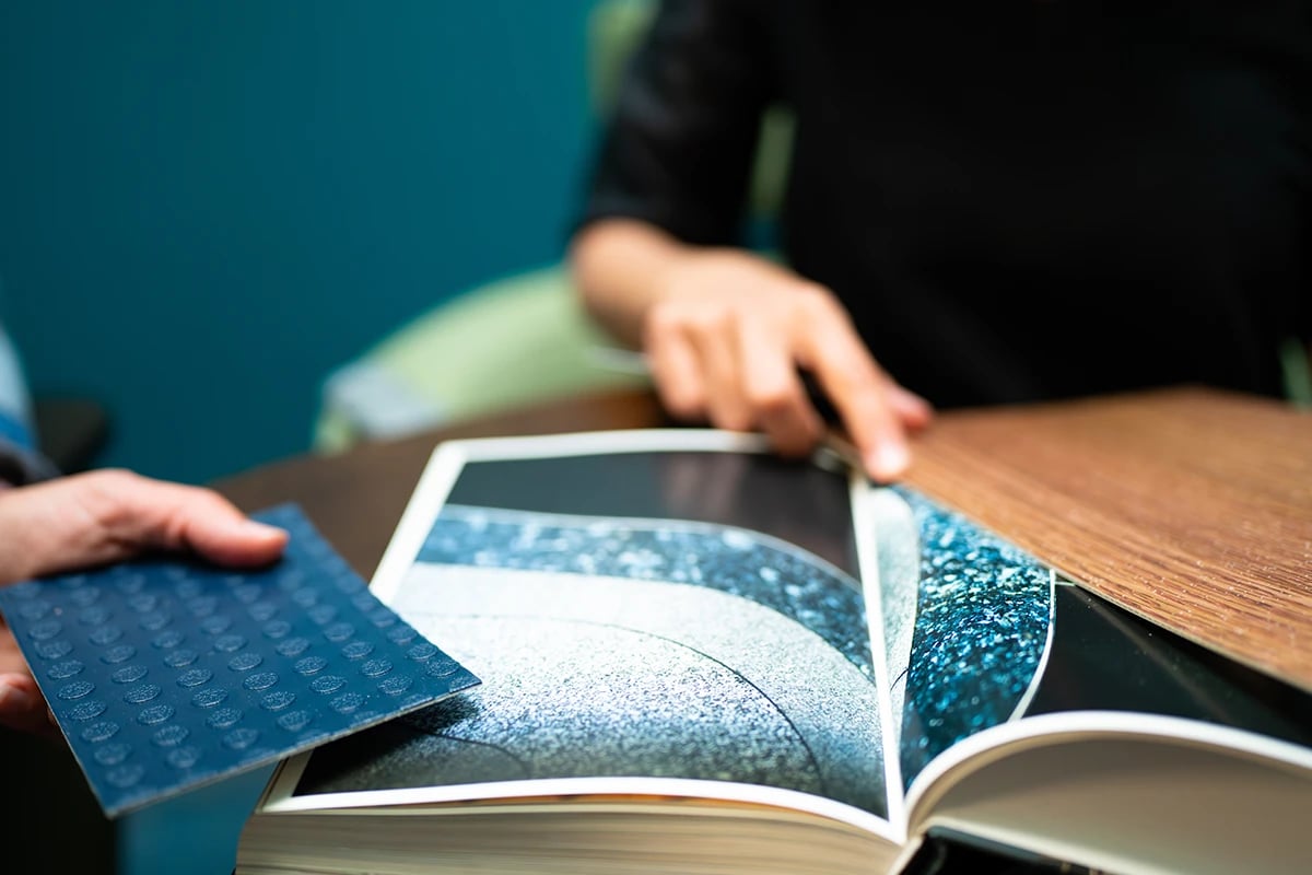 detailed-view-of-a-design-swatch-book-opened-on-a-table-flipped-to-a-design-with-two-people-holding-up-contrasting-laminate-swatches