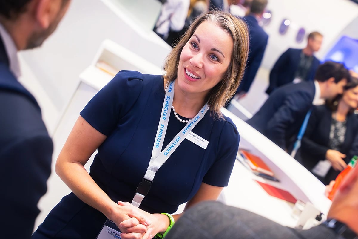 professionally-dressed-in-navy-blue-dress-schneller-employee-engaged-in-conversation-with-two-atendees-at-an-event