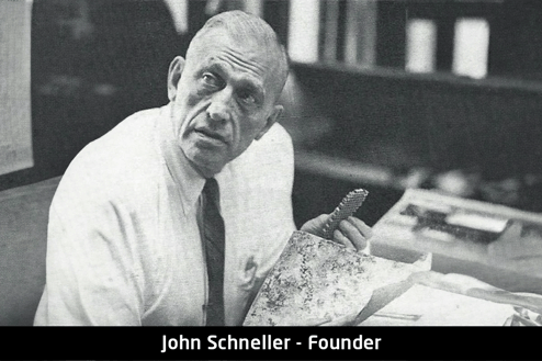 old-black-and-white-image-of-founder-john-schneller-sitting-in-chair-holding-aircraft-interior-material-focused-looking-up-at-camera