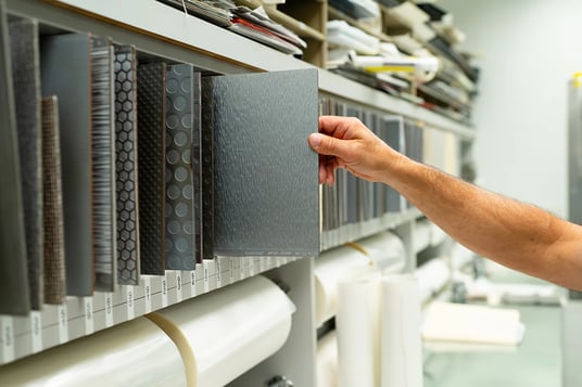 schneller-employee-hand-pulling-out-aircraft-flooring-swatch-off-of-a-texture-library-shelf