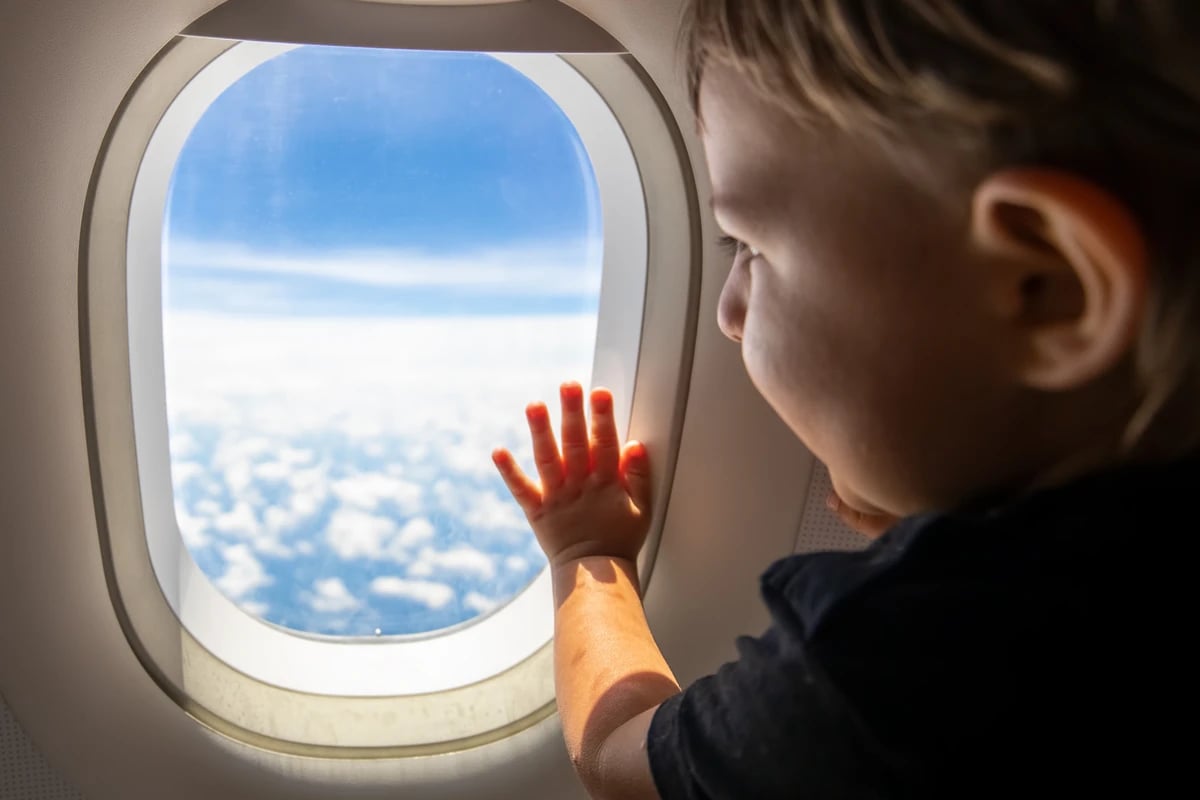 infant-looking-out-airplane-window-viewing-blue-sky-with-white-clouds