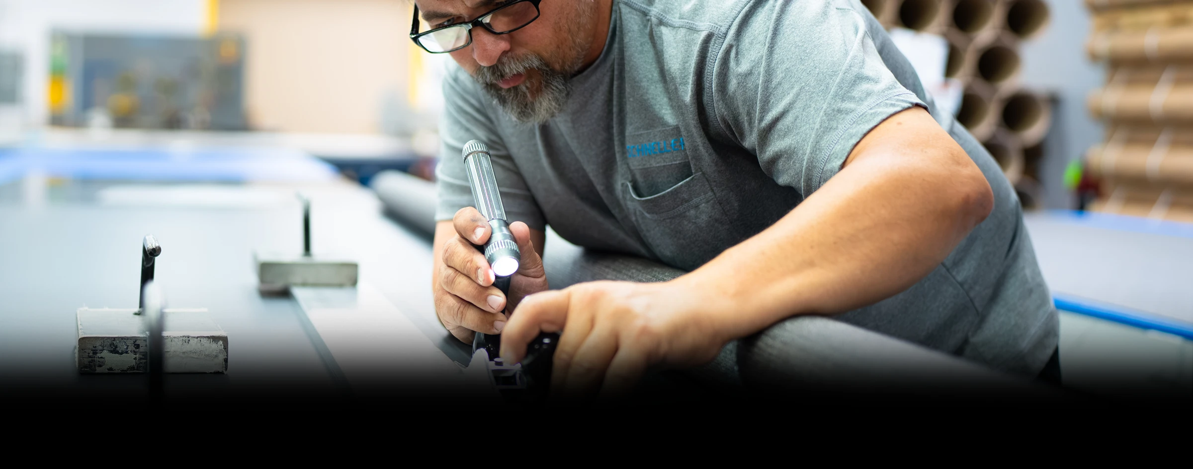 focused-schneller-employee-leaned-over-machine-inspecting-with-flashlight